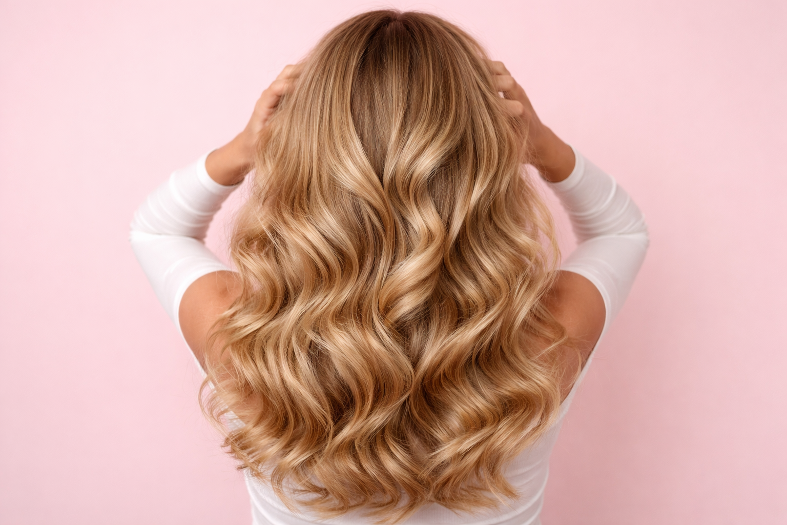 Volumineus blond haar tegen pastelroze achtergrond Achterkant van een vrouw met lang, volumineus, golvend blond haar tegen een pastel lichtroze achtergrond.